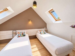 Een slaapkamer met twee bedden, een schuine plafond, een dakraam en een wandlamp.
