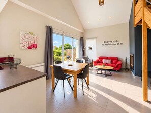 Een ruime woonkamer met een eettafel, rode bank en een groot raam met uitzicht op de omgeving.