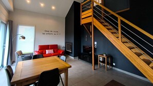 Uma sala de estar moderna com escada de madeira, um sofá vermelho, uma mesa de jantar e uma televisão.