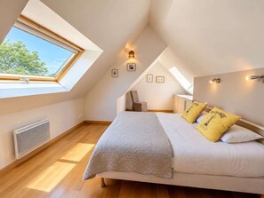 A bedroom with a skylight, a bed with pillows, a chair, and a small table.