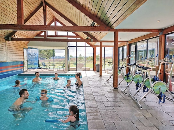 An indoor swimming pool with a wooden ceiling and exercise bikes.