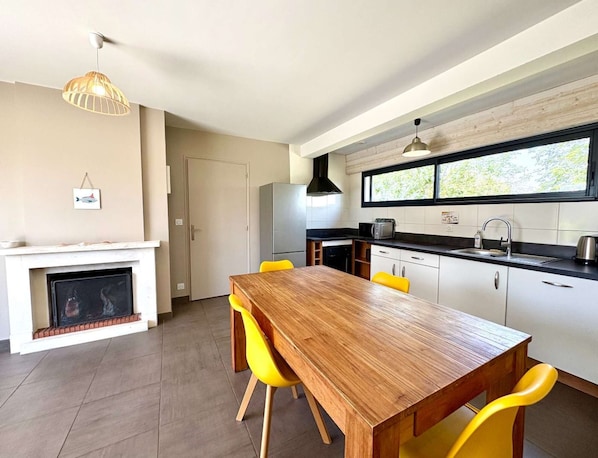 Une cuisine moderne avec une table à manger en bois et des chaises jaunes, un four encastré et une fenêtre donnant sur un espace verdoyant.