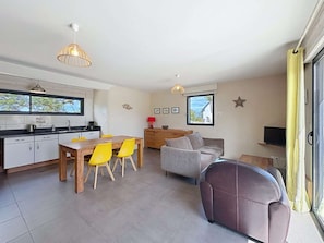 A modern kitchen with a dining area, a sofa, and a TV.