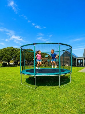 Ein Trampolin in einer grünen Wiese unter blauem Himmel.