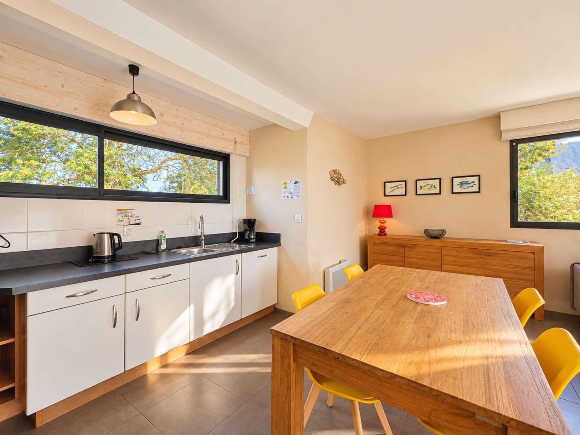 A modern kitchen with white cabinets, a wooden dining table, and yellow chairs.