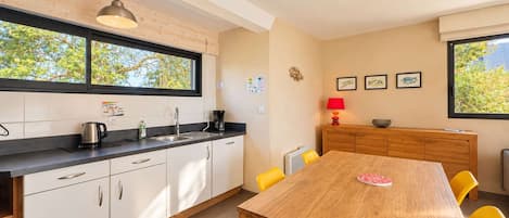 A modern kitchen with white cabinets, a wooden dining table, and yellow chairs.