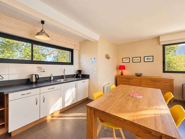 A modern kitchen with white cabinets, a wooden dining table, and yellow chairs.