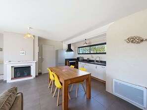 A modern kitchen with a dining area, a fireplace, and a window overlooking greenery.