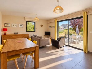 A spacious living area with a wooden dining table, yellow chairs, a grey sofa, and a television.
