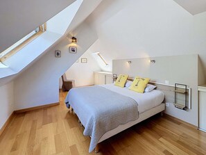 A bedroom with a sloped ceiling, a bed with a grey blanket, two pillows with text, a bedside table, and a wall-mounted light fixture.