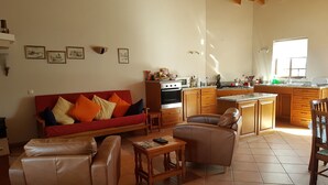Een ruime woonkamer met een rode bank, lederen fauteuils en een keuken met houten kasten en een aanrecht.