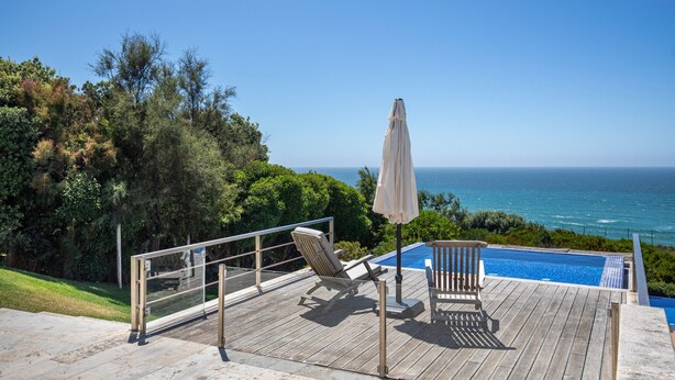 A wooden deck with a pool, lounge chairs, and an umbrella overlooking the ocean. - Luxury Beachfront Villa (Colares)