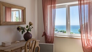A room with a wooden desk, a vase with flowers, a mirror, and a view of the sea through a window with sheer curtains. - Luxury Beachfront Villa (Colares)