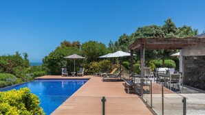 A swimming pool with a wooden deck, lounge chairs, and umbrellas. - Luxury Beachfront Villa (Colares)