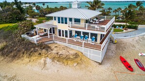 Une maison de deux étages située en bord de mer, dotée d’un balcon, d’une piscine et de kayaks sur le sable.