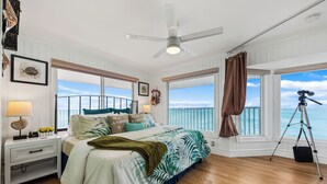 A bedroom with a large bed, a ceiling fan, and a view of the ocean.