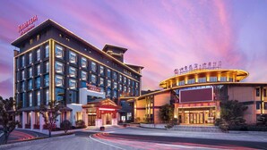Un hotel moderno con un llamativo letrero de "Ramada", que cuenta con una amplia entrada, varios pisos y una fachada bien iluminada.