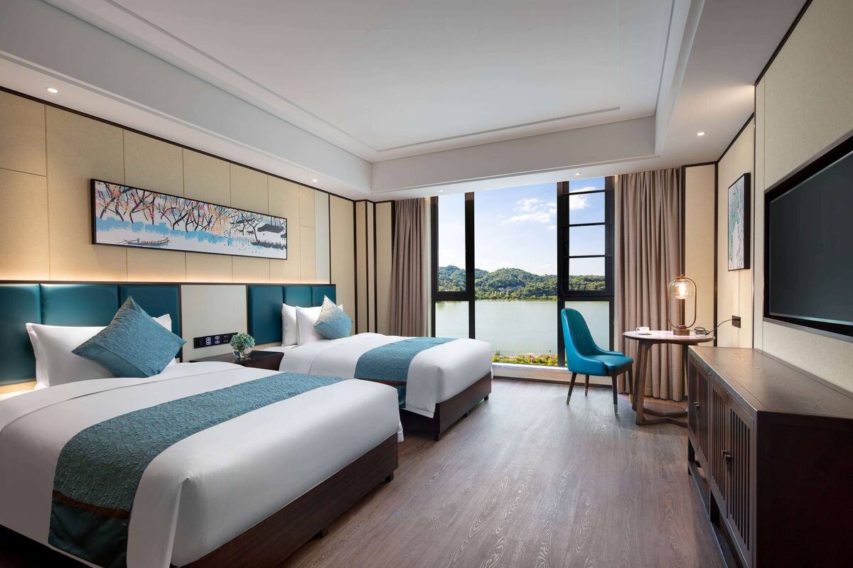 Ein Hotelzimmer mit zwei Betten, einem Fernseher, einem Schreibtisch und Blick auf einen See.