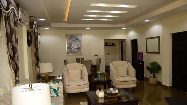 A modern living room with a sofa, two armchairs, a coffee table, and a lamp. There is a painting on the wall and a potted plant. - Marshall Hotel Apartments (Kano)
