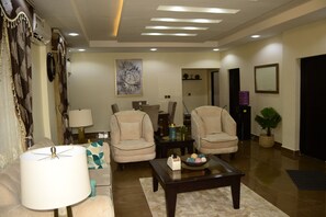 A modern living room with a sofa, two armchairs, a coffee table, and a lamp. There is a painting on the wall and a potted plant. - Marshall Hotel Apartments (Kano)