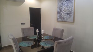 A dining table with four chairs, a candle holder, and a framed floral artwork on the wall. - Marshall Hotel Apartments (Kano)