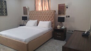 A neatly made bed with a tufted headboard, two bedside tables with lamps, and a small bedside table with a tissue box. - Marshall Hotel Apartments (Kano)