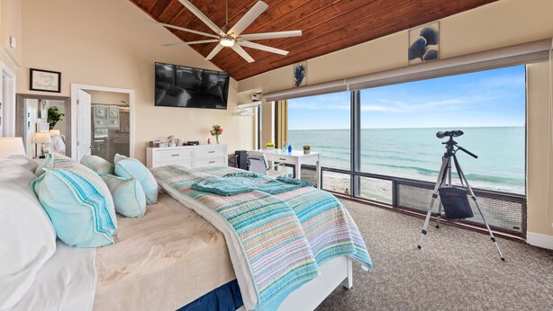 A bedroom with a large bed, a ceiling fan, a TV, and a view of the ocean.