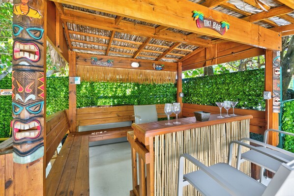 Un espace bar extérieur avec des meubles en bois, un toit de chaume et un décor sur le thème des tropiques.