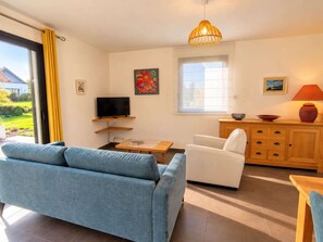 A living room with a sofa, a television, a dining table, and a window with curtains.