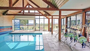 Zona de piscina cubierta con bicicletas de ejercicio y vistas al exterior.