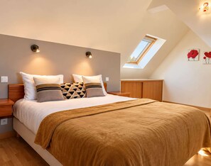 A bedroom with a bed, two bedside tables, a nightstand, a wooden wardrobe, a skylight, and two wall-mounted lamps.