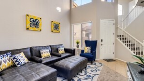 A living room with a black leather sofa, a blue armchair, and a white door. - Group Luxury Retreat ~ 4 Neighboring Homes, 21 Beds, Pool & Golf Community (Mesa)