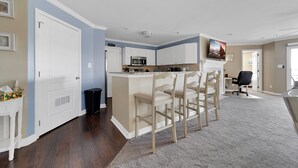 A modern kitchen with white cabinets, a central island with bar stools, a microwave, and a sink.