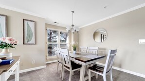A dining room with a table and chairs, a chandelier, a mirror, and a window with blinds.
