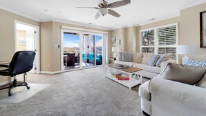 A spacious living room with a ceiling fan, a white sofa, a coffee table, and a black office chair.
