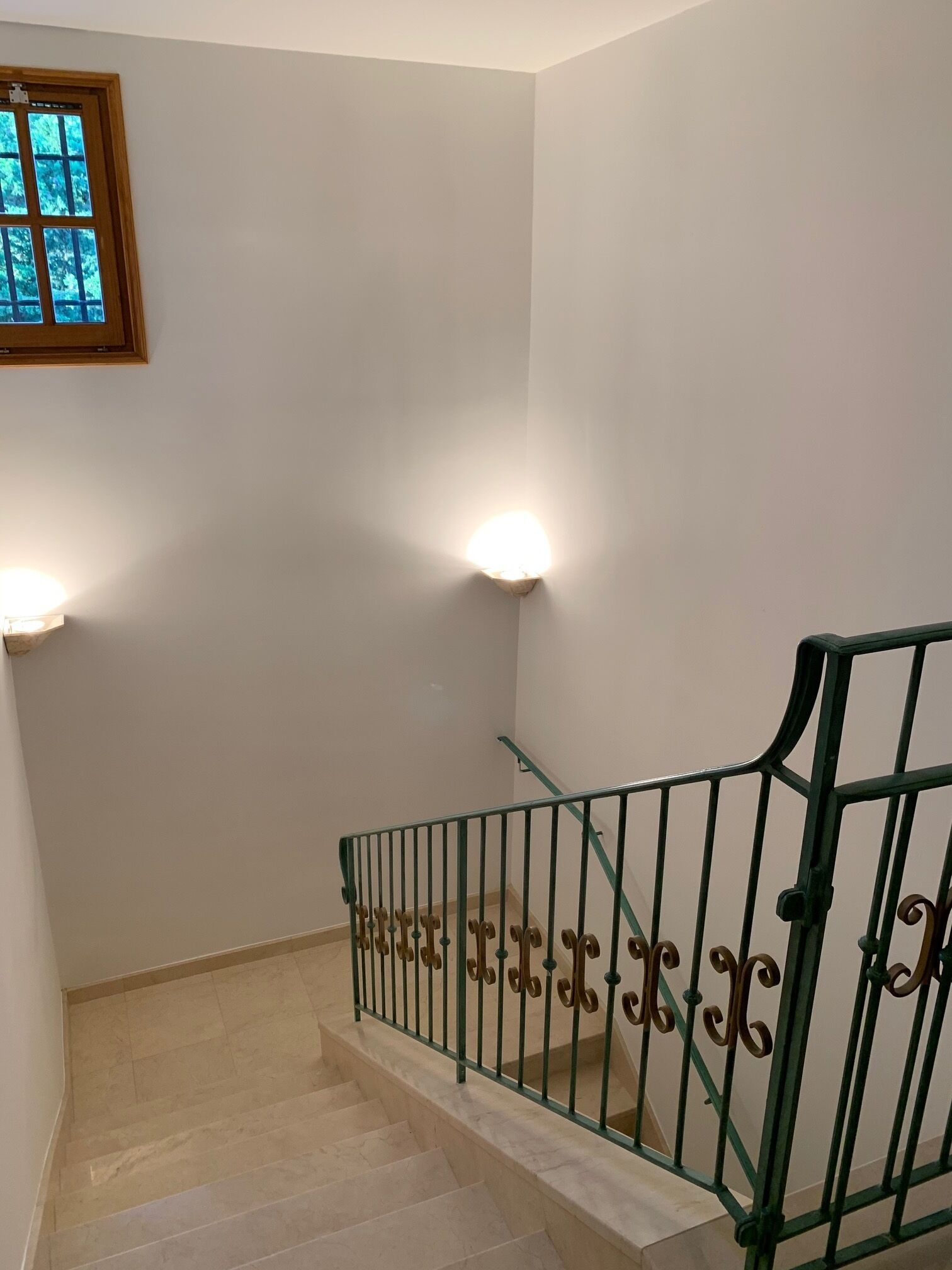 A staircase with a green metal railing, white walls, and two wall-mounted lights.