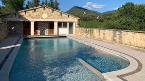 Un bâtiment en pierre doté d’une piscine, entouré de verdure et de collines.