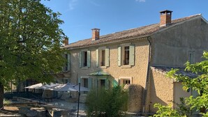 Un bâtiment en pierre doté d’une cour, d’un espace extérieur aménagé avec des sièges et d’un arbre.