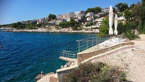 A coastal area with a clear blue sea, a rocky shoreline, and a row of white buildings in the background. - Apartment Nina - Large 2 bedroom Apt  250m Beach amenities 100m Free Parking (Split)