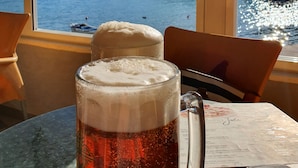A glass of beer with a frothy head, placed on a table with a menu beside it, overlooking a body of water with buildings in the background. - Apartment Nina - Large 2 bedroom Apt  250m Beach amenities 100m Free Parking (Split)