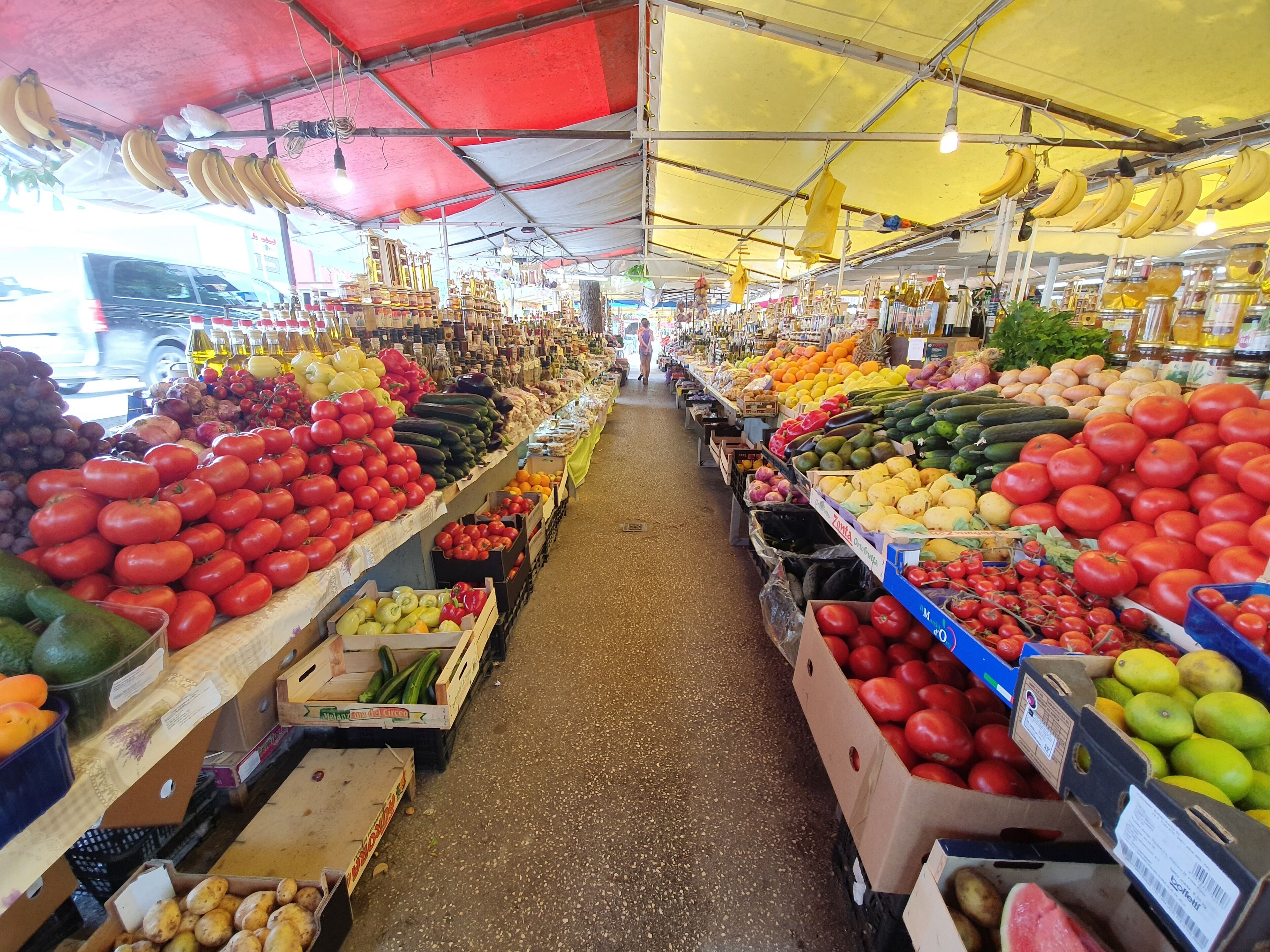 Ein überdachter Markt mit verschiedenen Früchten und Gemüsesorten, präsentiert auf Tischen und Regalen.