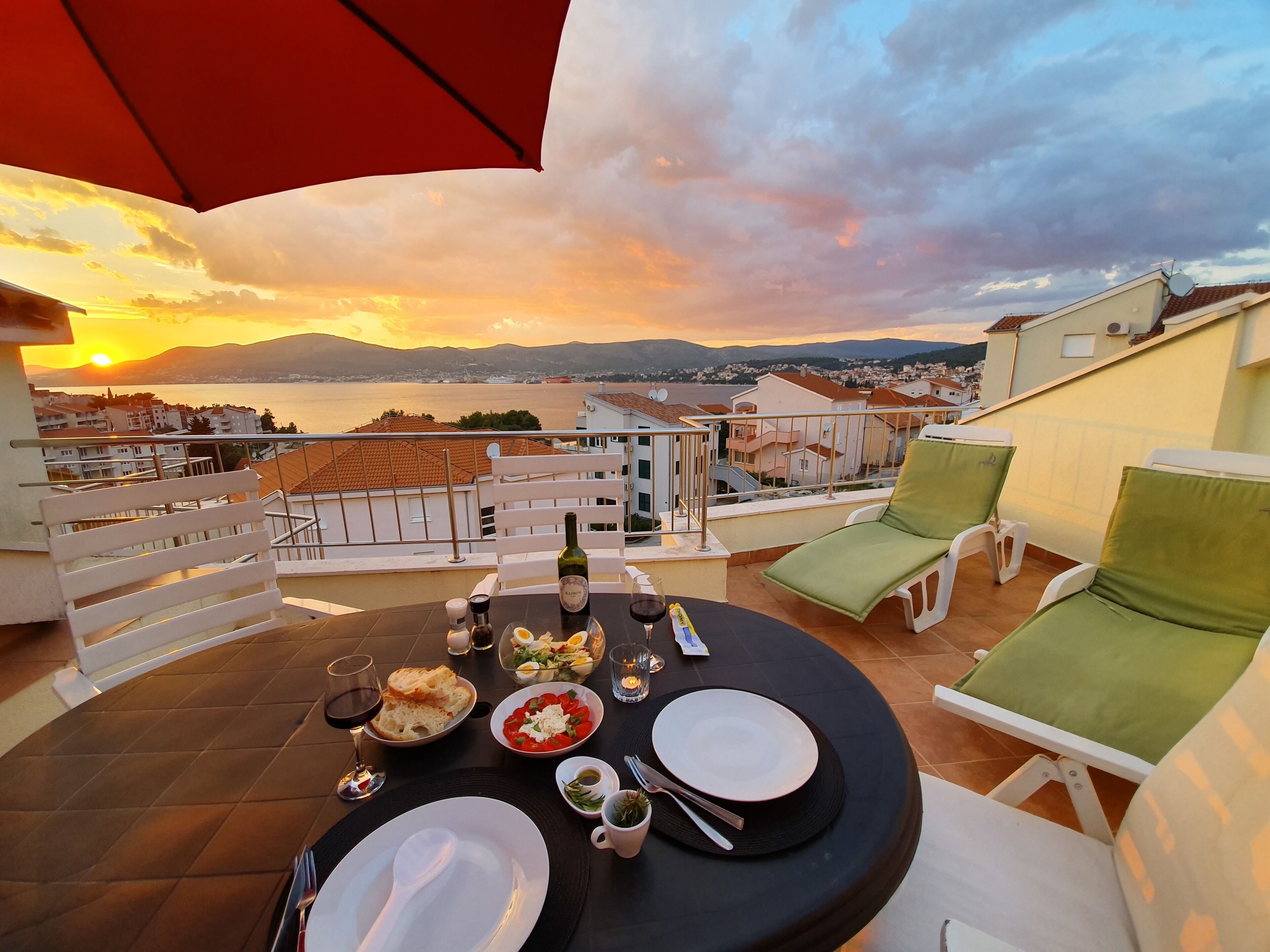 Eine Dachterrasse mit gedecktem Tisch, mit Blick auf eine malerische Wasserlandschaft und ferne Berge.