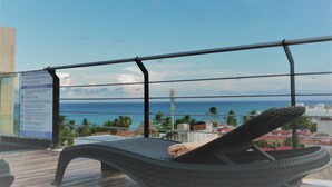 A balcony with a view of the ocean, a lounge chair, and a metal railing. - Sole Suites Playa del Carmen (Playa del Carmen)