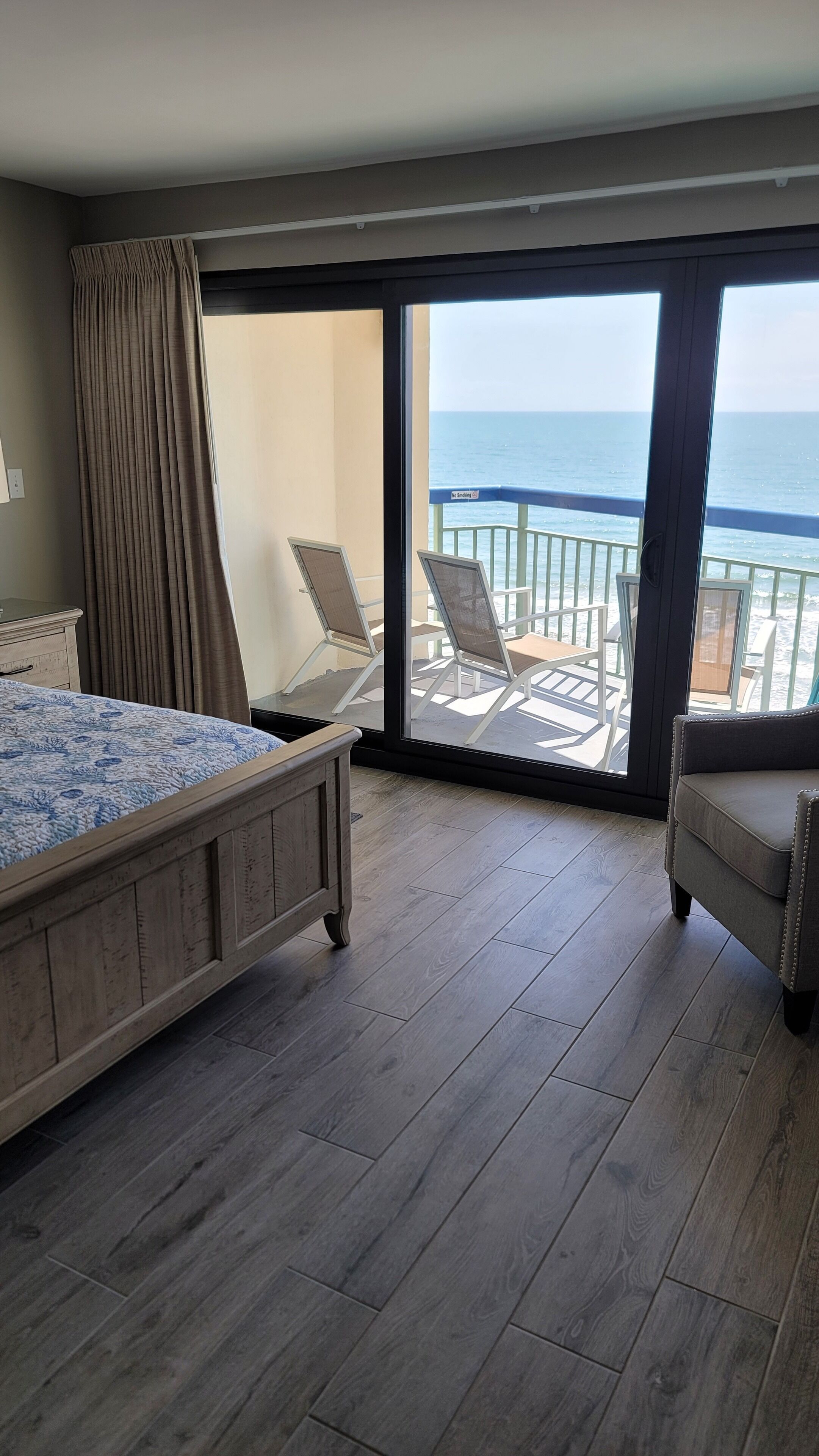 Une chambre avec un lit, un balcon donnant sur la mer et un coin salon avec des fauteuils.