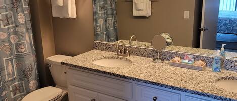 A bathroom with a granite countertop, a white toilet, a vanity with drawers, and a shower curtain with a sea shell pattern.
