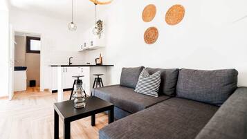 Un saló modern amb un sofà gris, una taula de cafè negra i una zona de cuina al fons.