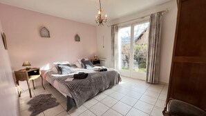 Un dormitorio con cama, mesita de noche, lámpara, silla y vista al exterior a través de una ventana.