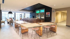 A modern bar area with a long counter, bar stools, and a television screen displaying sports. - Courtyard by Marriott Cartersville (Cartersville)