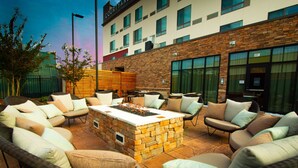A courtyard with wicker furniture, a stone fire pit, and a building with a stone facade and multiple windows. - Courtyard by Marriott Cartersville (Cartersville)