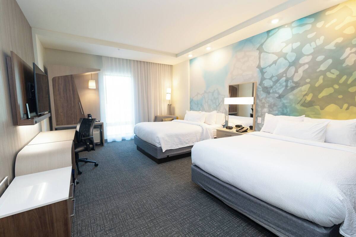 Une chambre d’hôtel avec deux lits, un bureau, une chaise, une télévision et un tableau au mur.